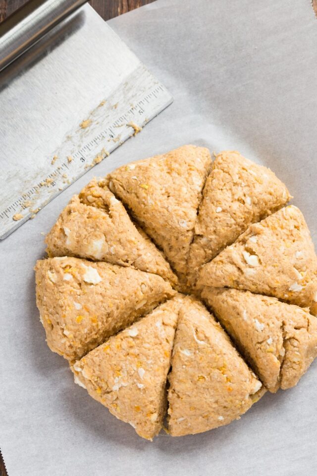 Scone dough shaped in a round disc and cut into triangles on white parchment paper.