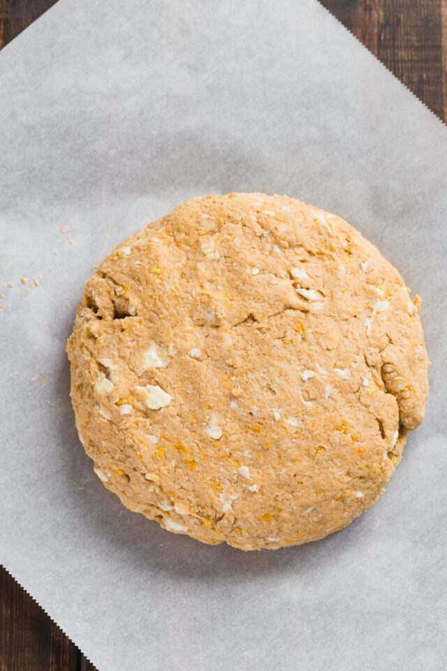 Scone dough shaped in a round disc on white parchment paper.