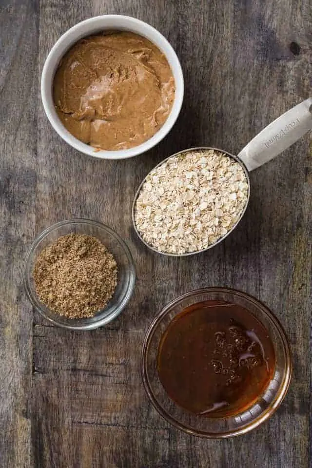 Almond butter, oats, flaxseed meal, and honey arranged in bowls on a wooden surface.