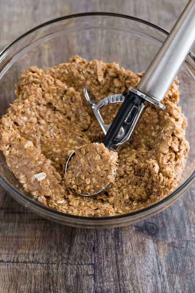 Almond butter and oats mixed together in a glass bowl being scooped out with a cookie scoop.