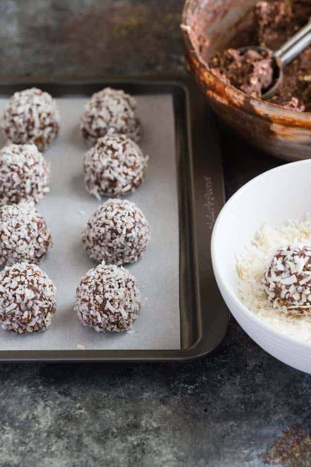 A pan of chocolate peanut butter balls coated in coconut sitting next to a bow of batter and a bowl of coconut.
