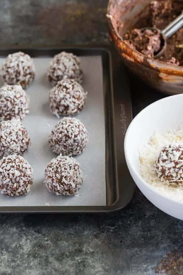 Chocolate Peanut Butter Oatmeal Balls with Coconut A pan of chocolate peanut butter balls coated in coconut sitting next to a bow of batter and a bowl of coconut.