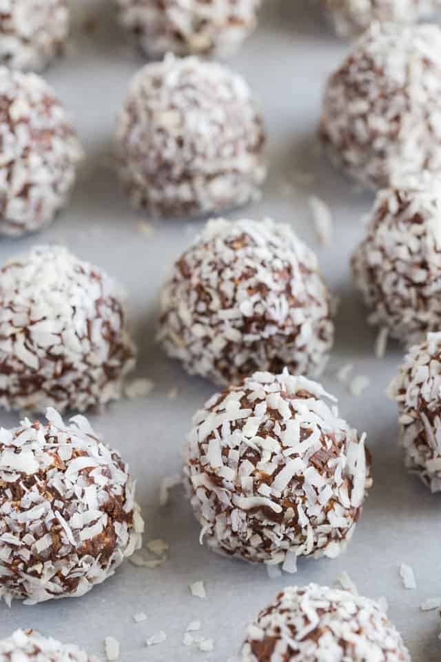 Chocolate peanut butter oatmeal balls with coconut lined neatly on a baking sheet covered in white parchment paper.