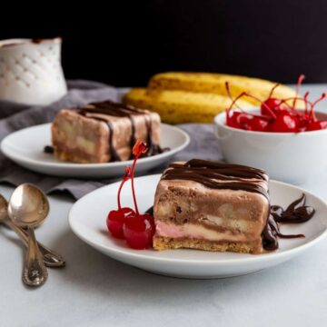 side view of a slice of no-bake banana split cake on a white plate with cherries