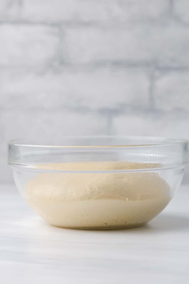 A ball of dough rising in a glass bowl