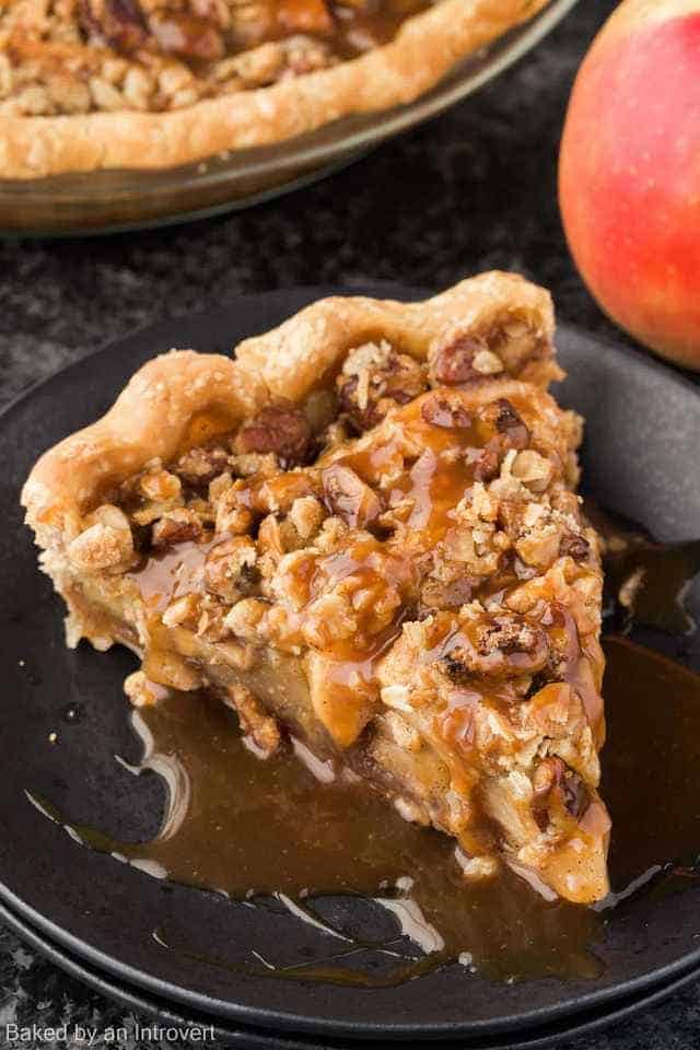 A slice of caramel apple pecan streusel pie on a black plate.