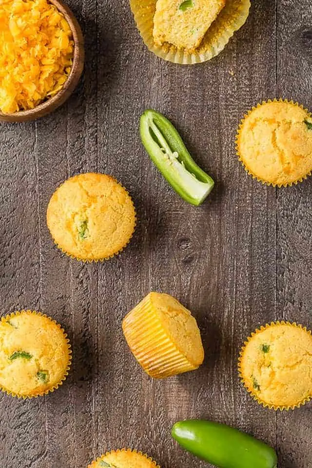 Overhead view of cheddar jalapeno cornbread muffins with a bowl of cheddar cheese and jalapenos.