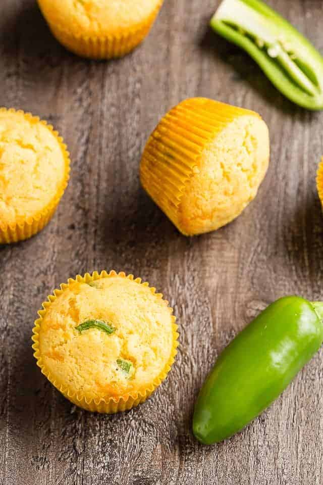 Cheddar Jalapeno Cornbread Muffins and whole jalapenos on a wooden table.