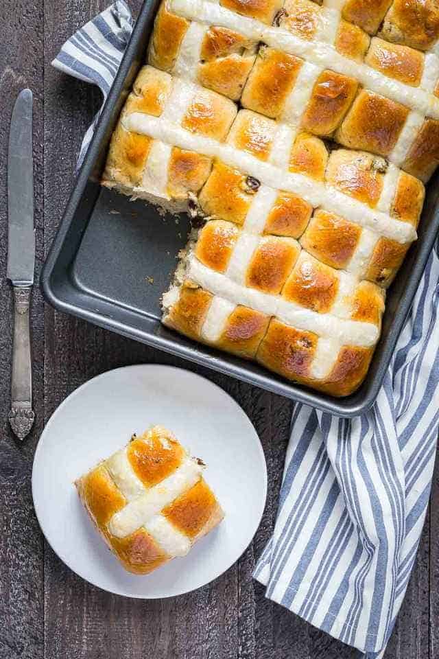 pan of Hot Cross Buns with one taken out and placed on a plate