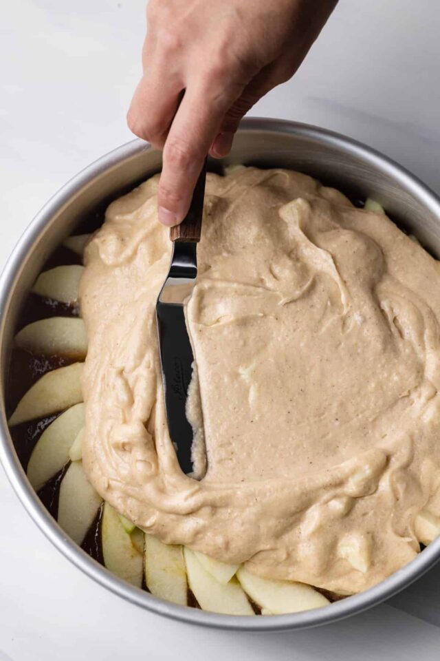 Spiced apple cake batter being spread over apple slices in a cake pan