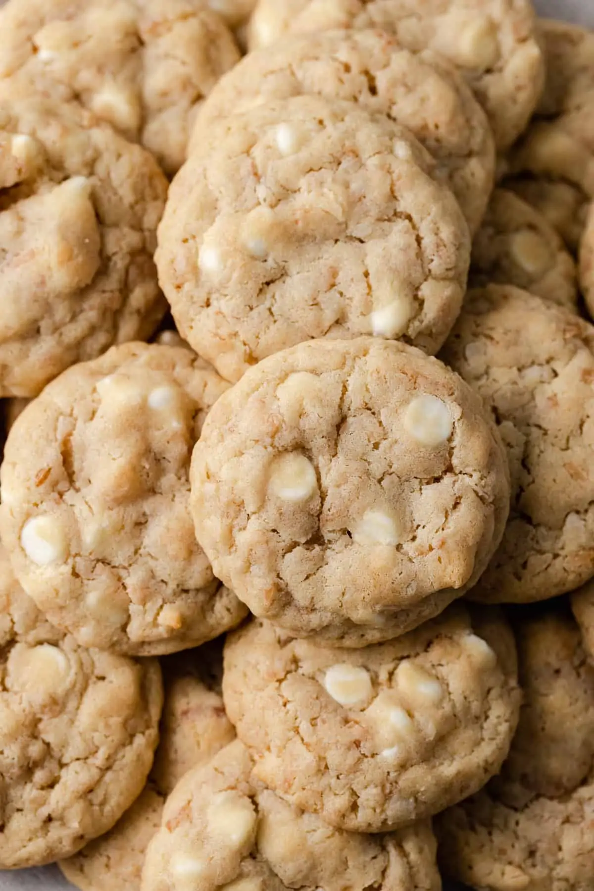 closeup overhead view of white chocolate chip cookies with toasted coconut on white parchment paper