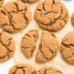A close up view of chewy gingersnap cookies broken in half on a pieces of brown parchment paper.