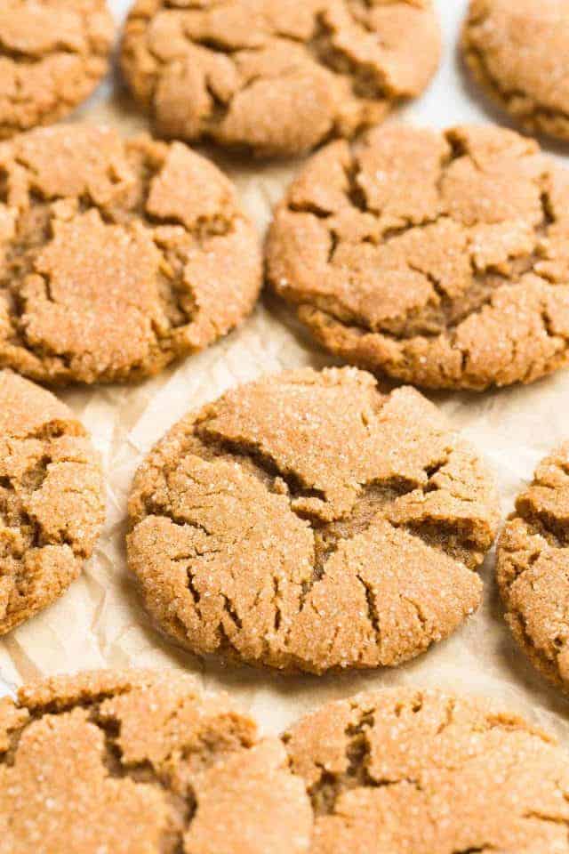 A close up view of chewy gingersnap cookies with crackly tops on a pieces of brown parchment paper.