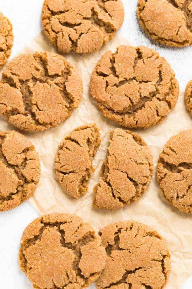 A close up view of chewy gingersnap cookies broken in half on a pieces of brown parchment paper.