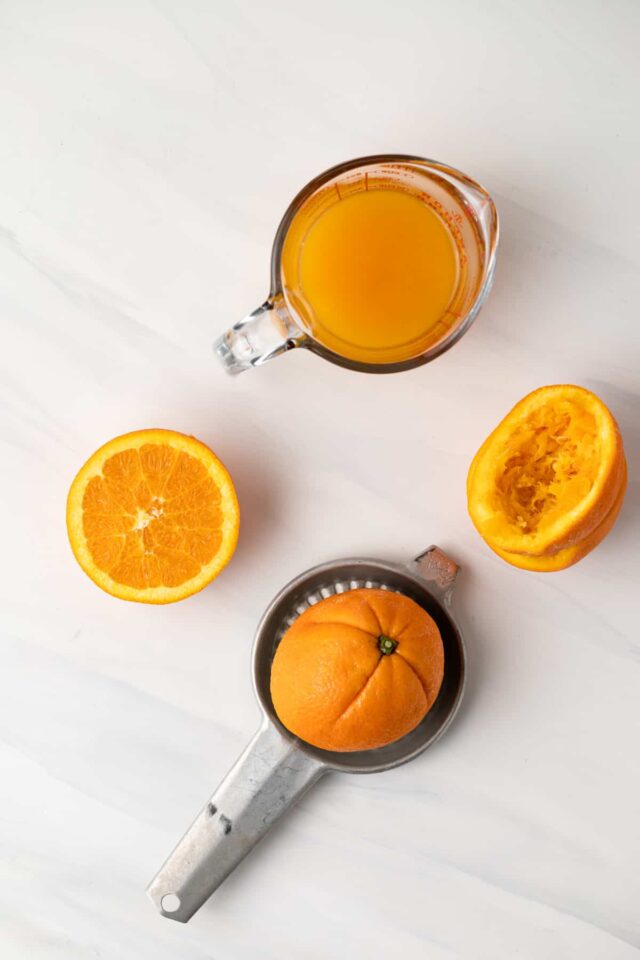 Four orange halves being squeezed in strainers