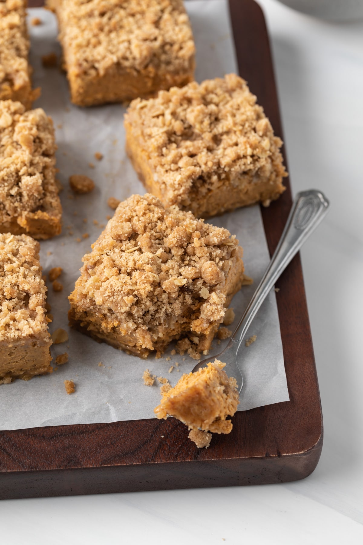 pumpkin bars on parchment lined cutting board with a fork taking a bite out of one