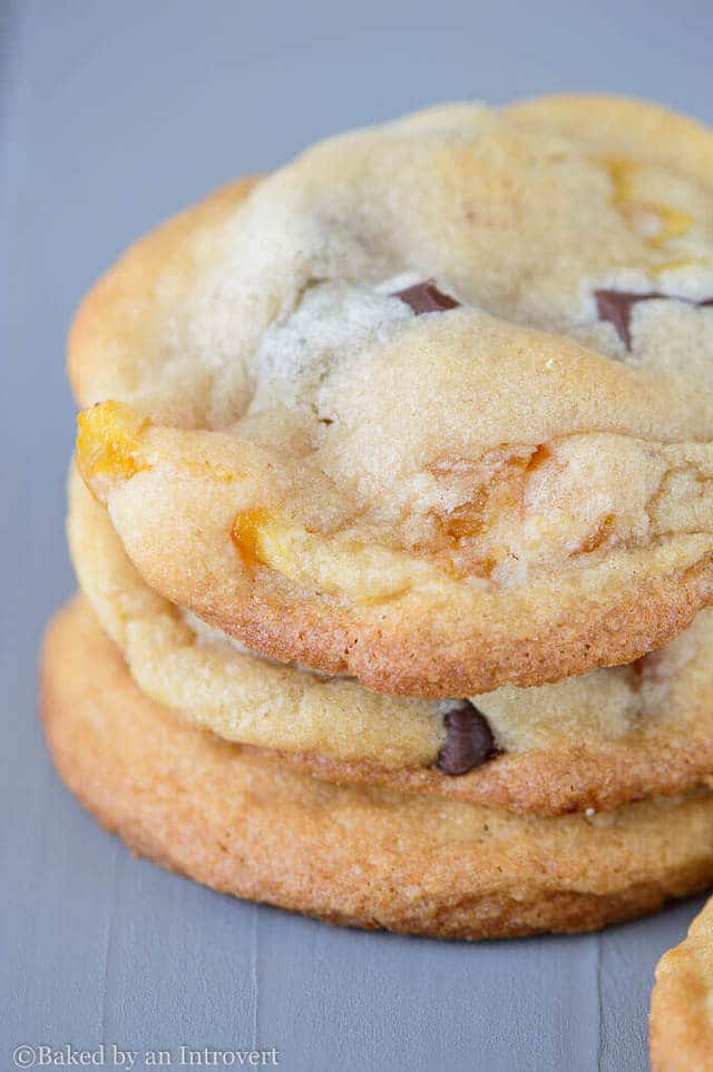 three chocolate chunk apricot cookies stacked on a gray background