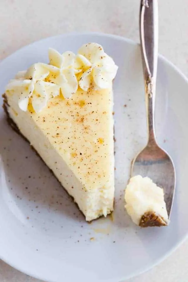 Overhead view of a slice of Eggnog Cheesecake on white plate with a fork taking a bite out.