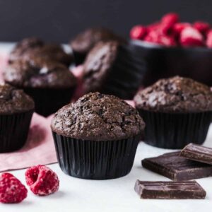Double chocolate muffins with raspberries on a white tabletop with a pink napkin.