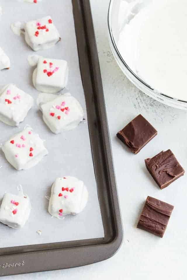 Plain and white chocolate coated fudge on a baking sheet with a bowl of white chocolate next to it.