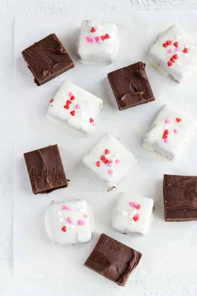 Hot chocolate fudge coated in white chocolate and topped with heart sprinkles on a piece of white parchment paper.