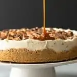 no bake snickers cheesecake with caramel drizzle on a white cake stand