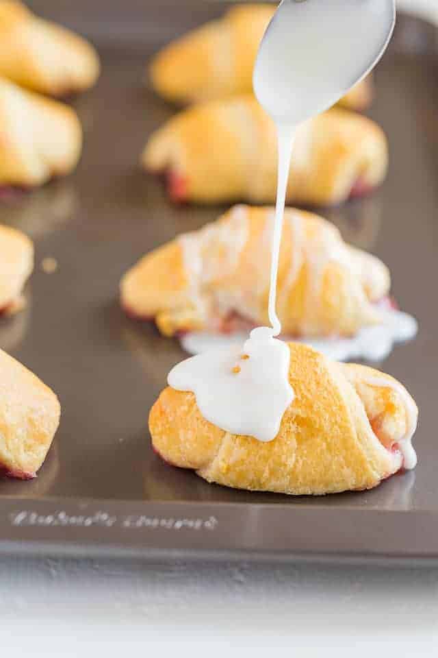 lemon glaze being drizzle over crescent rolls with a spoon