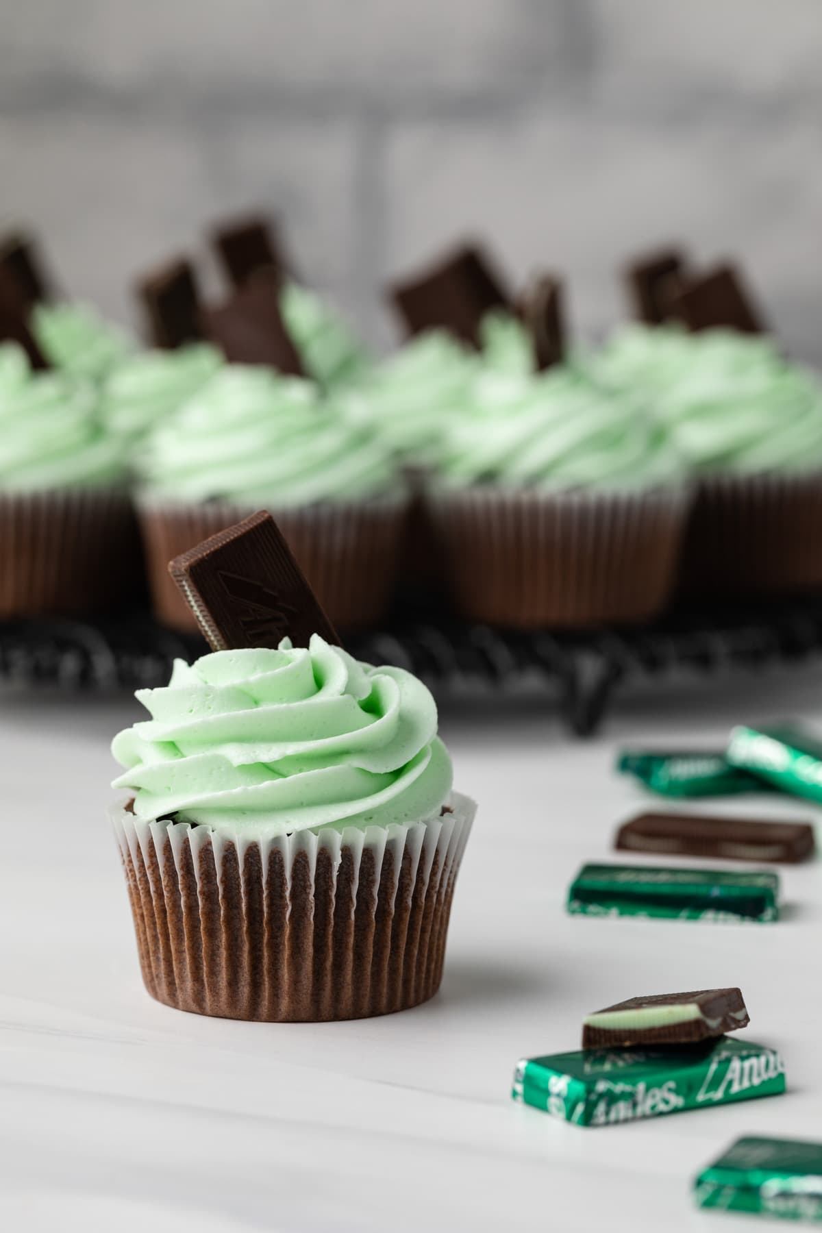 Andes mint cupcakes on wire rack with one in front.