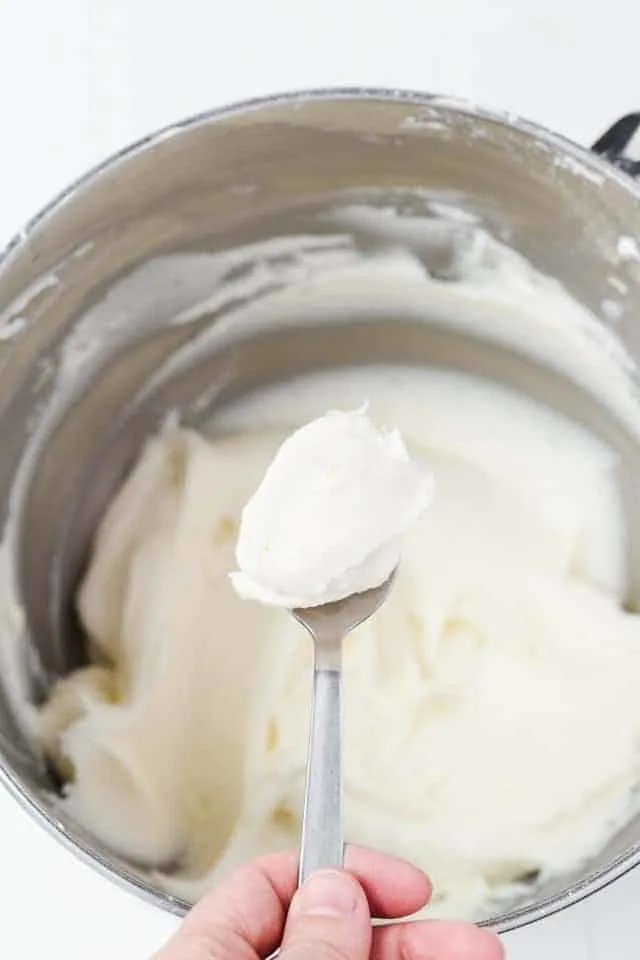 Coconut buttercream frosting on a spoon held over a bowl of frosting.