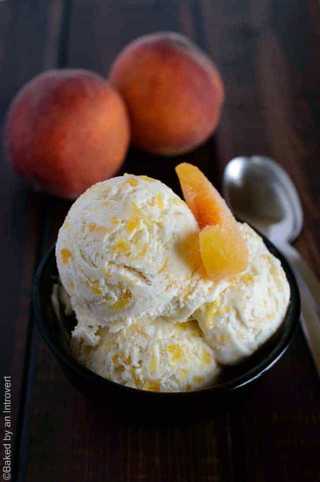 Angled view of peaches and cream ice cream in a black bowl with a sliced peach on top.