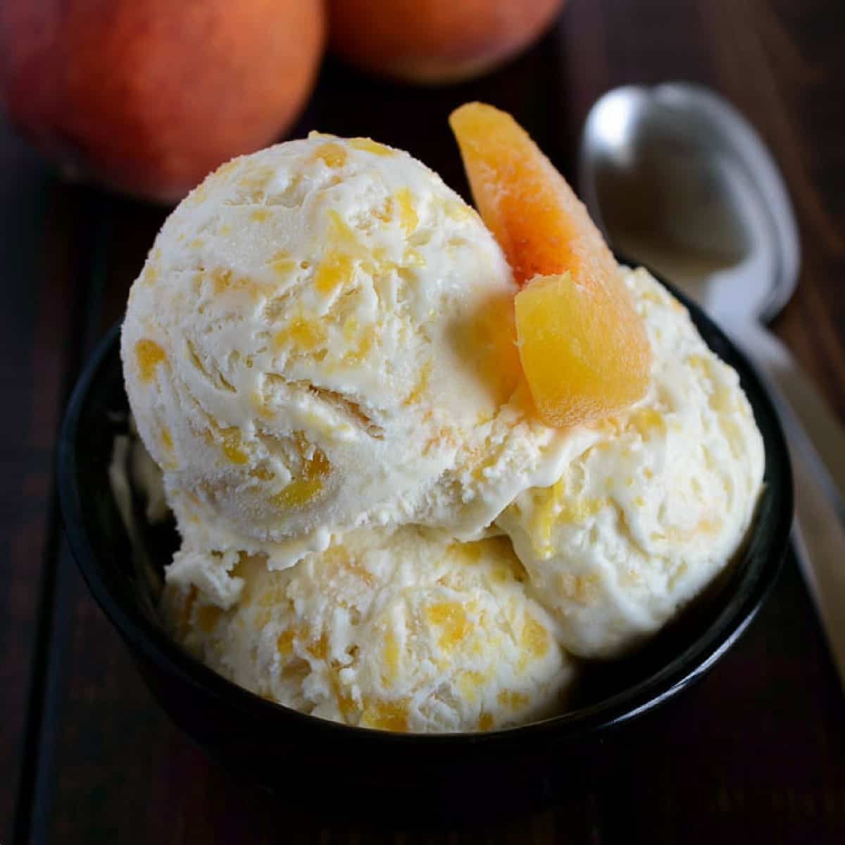 Angled view of peaches and cream ice cream in a black bowl with a sliced peach on top.