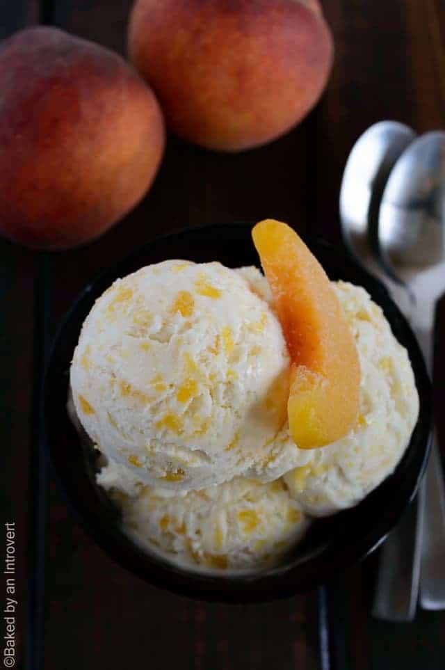 Scoops of peaches and cream ice cream in a black bowl with a slice peach on top.