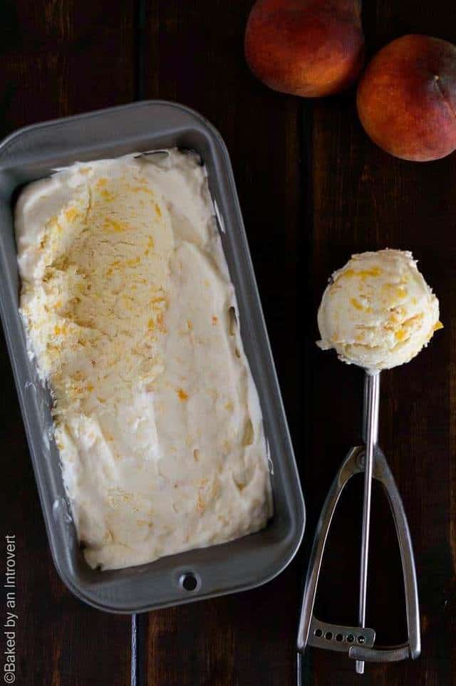 Peaches and cream ice cream in a loaf pan with a scoop next to it.