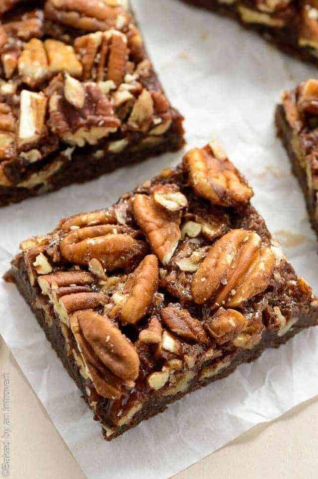 A close up view of a chocolate bourbon pecan bar on a piece of white parchment paper.