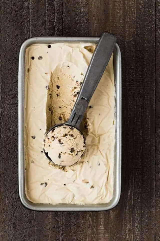 Coffee crunch ice cream in a loaf pan with a scoop taking out a scoop.