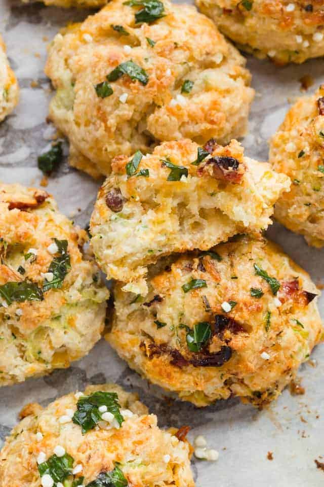 cheddar zucchini drop biscuits on white parchment paper with one broken so the inside is visible