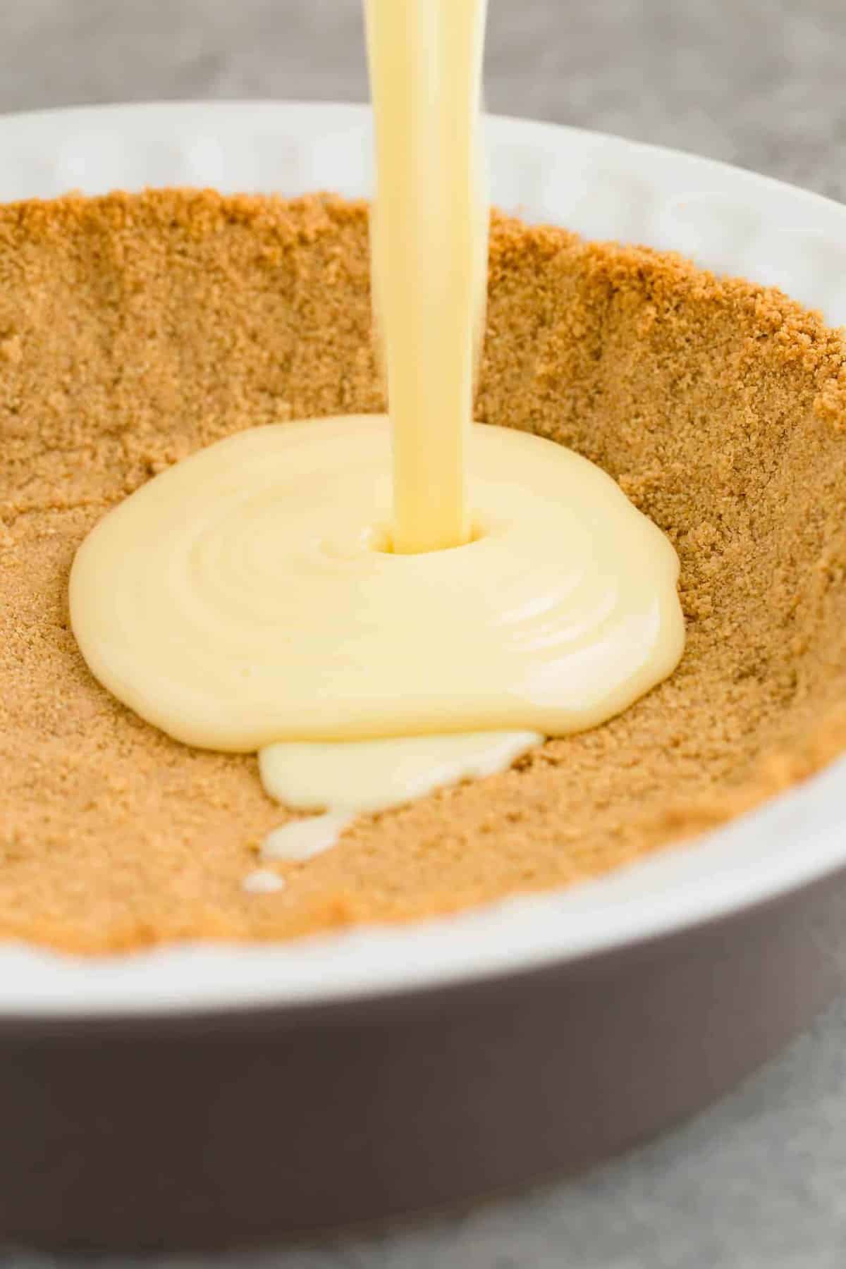 Lime pie filling being poured into a graham cracker crust.