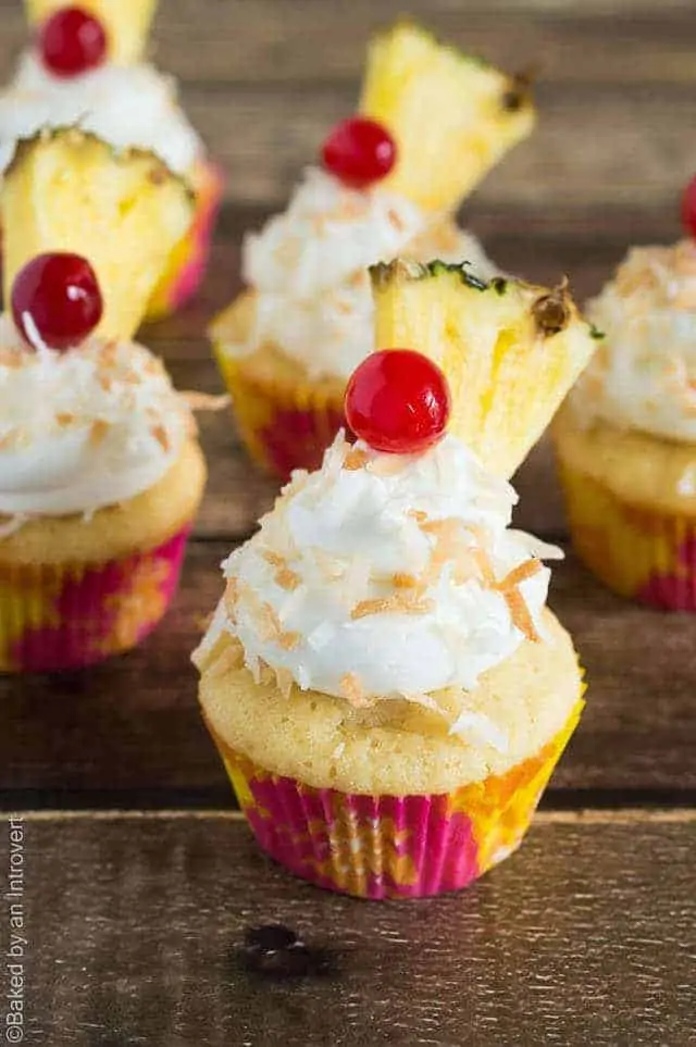 Angled view of pina colada cupcakes on wood background.