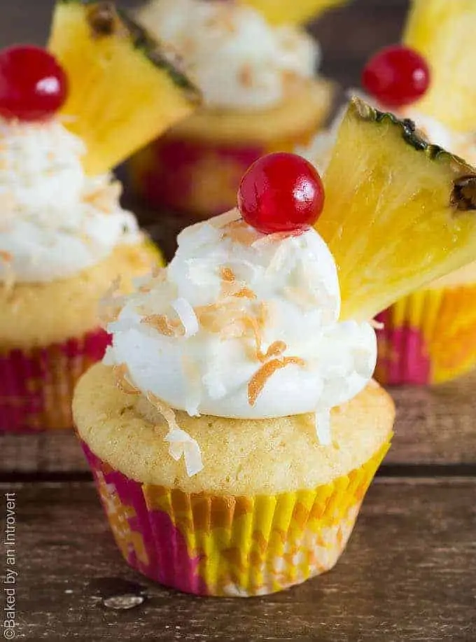 Side view of pina colada cupcakes with coconut frosting, a cherry, and pineapple slice on top.