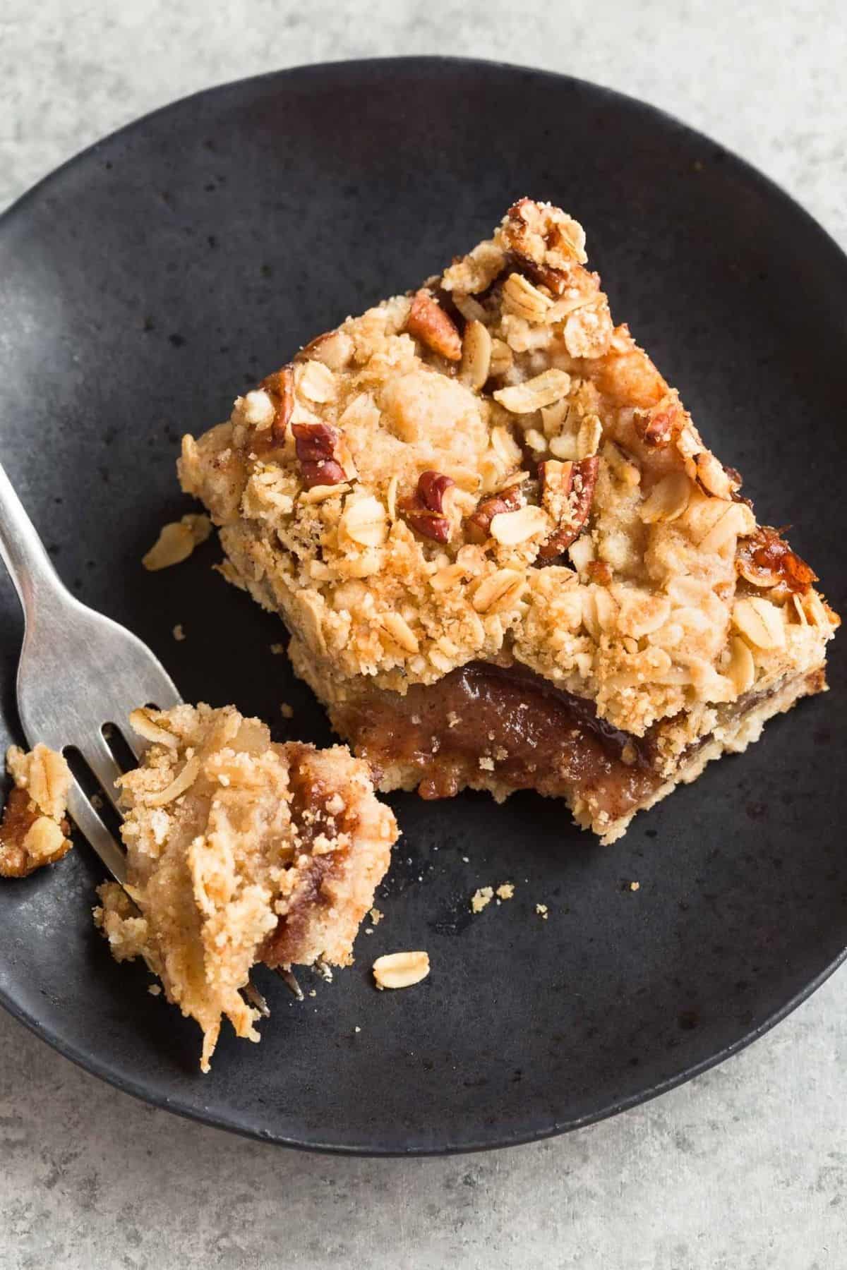 Apple Streusel Bar on a black plate with a fork taking a bit out of it.