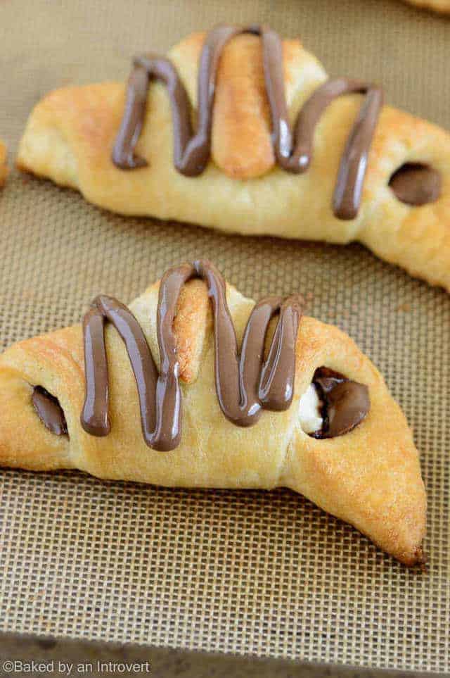 Two Nutella cream cheese crescent rolls on a baking sheet lined with parchment paper.
