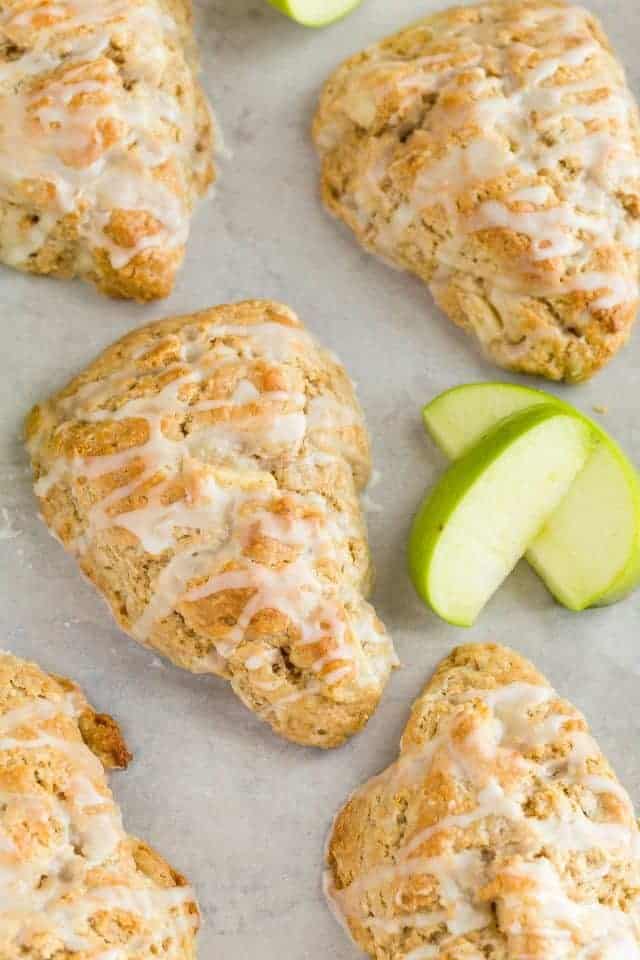 A close up view of an apple cinnamon scone on a parchment lined baking sheet with slices of green apple next to the scone.
