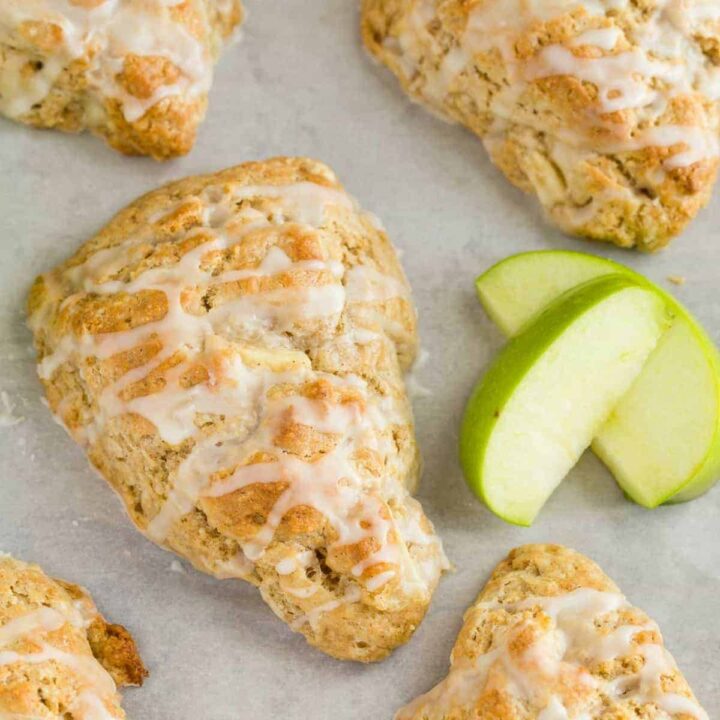 A close up view of an apple cinnamon scone on a parchment lined baking sheet with slices of green apple next to the scone.