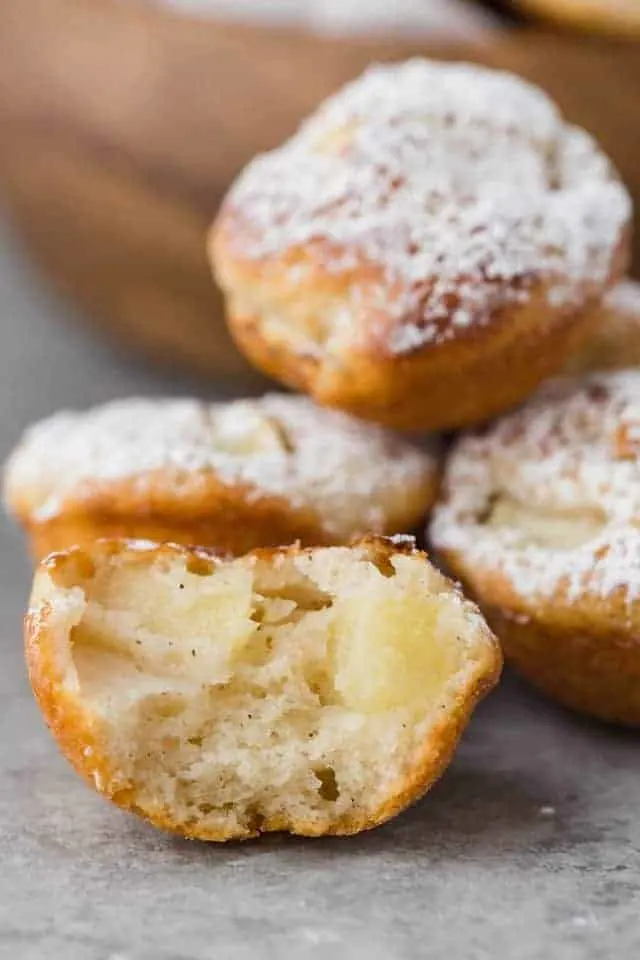 Close up view of a baked apple fritter that's cut in half so you can see the fluffy interior speckled with chunks of apples.