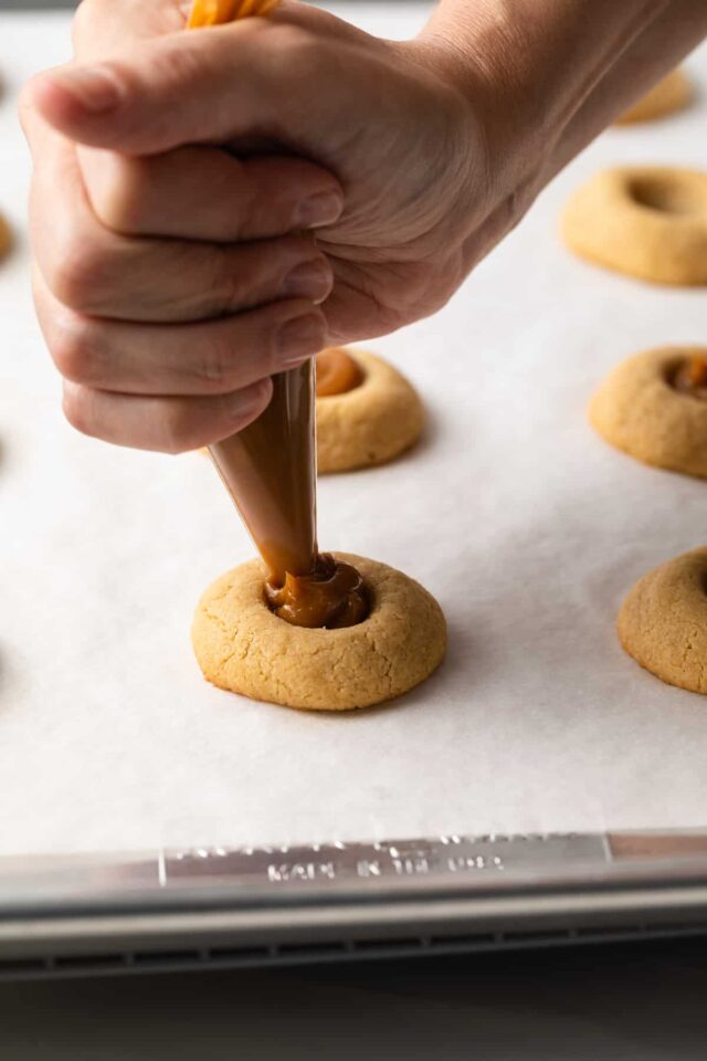 Dulce de leche being added to the center of thumbprint cookies