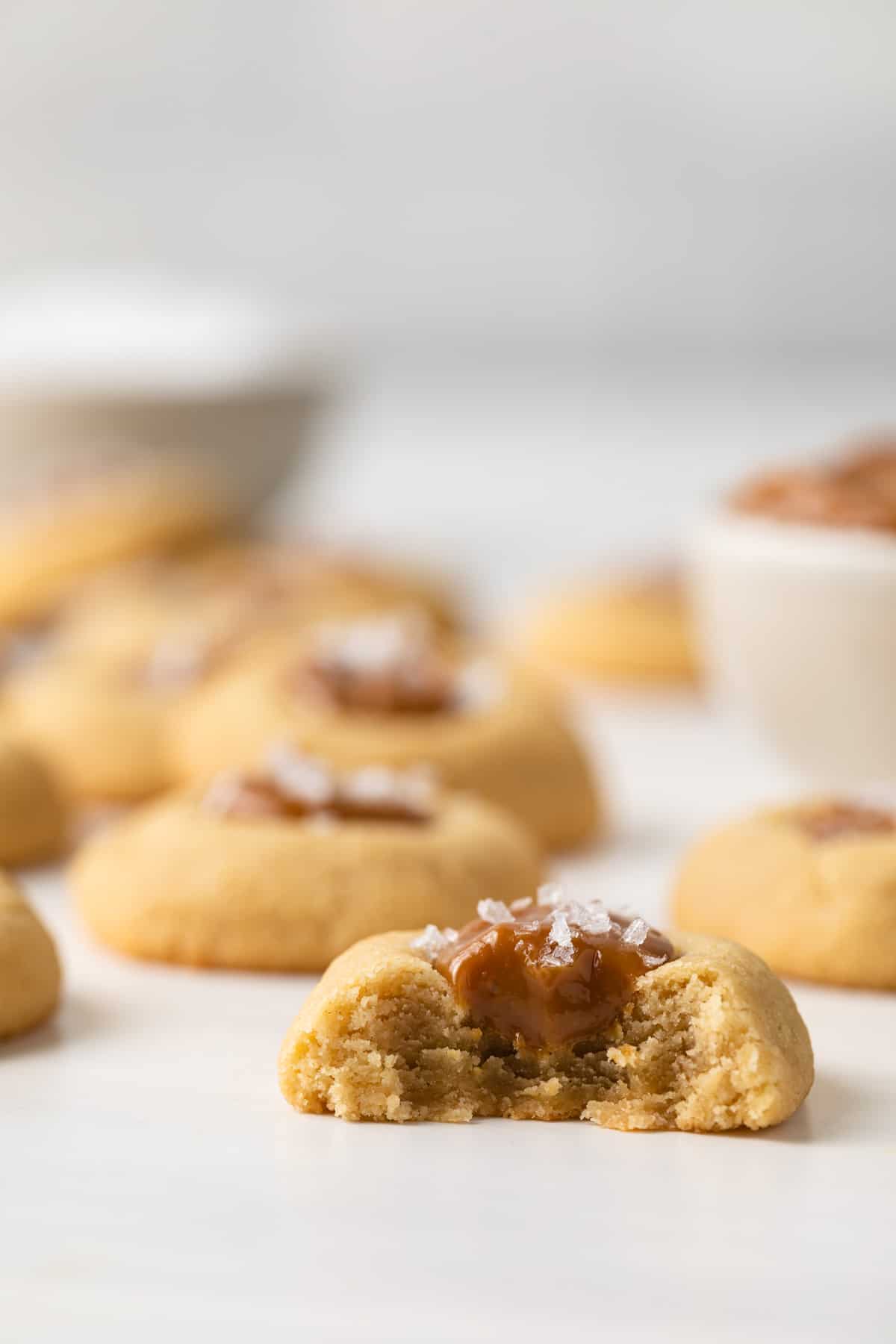 A dulce de leche thumbprint cookie with a bite missing and other cookies in the background