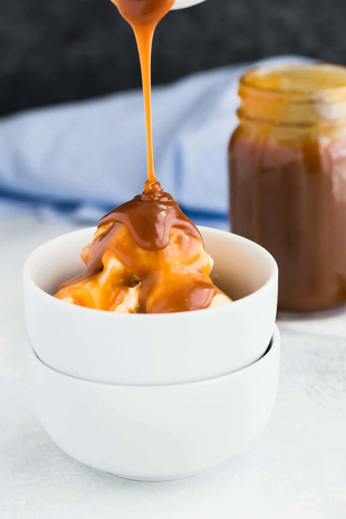 Homemade caramel sauce bring drizzled over a scoop of ice cream in a white bowl.
