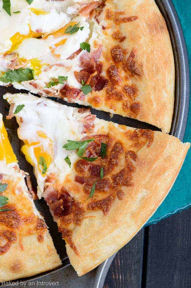Close up view of a Bacon Egg Breakfast Pizza with a slice slightly pulled away.