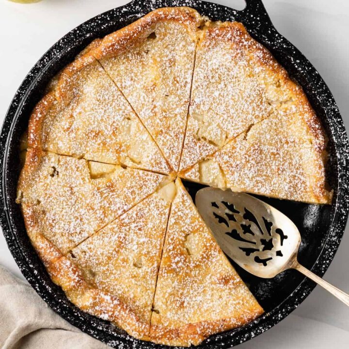 Overhead view of maple pear clafoutis in a cast iron skillet with a slice taken out.