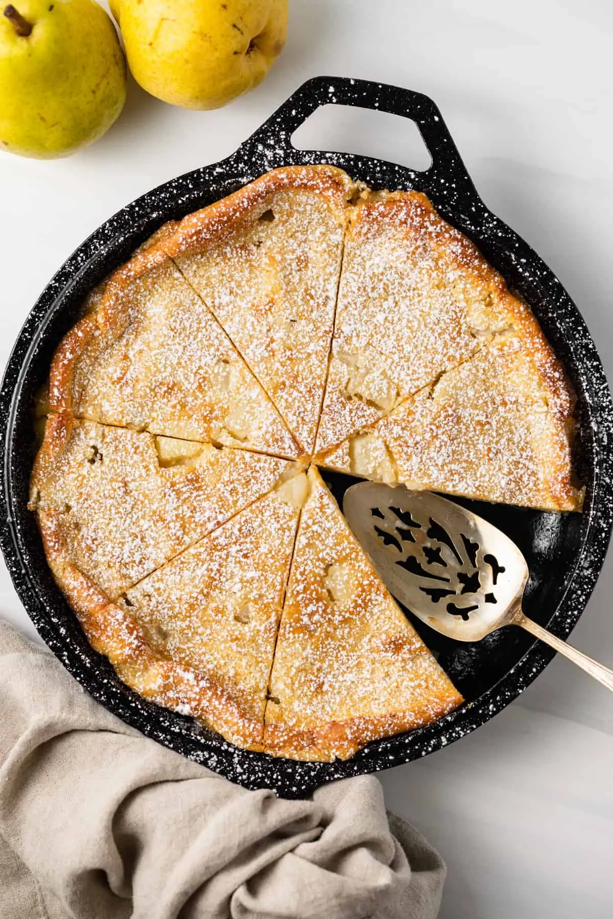 Overhead view of maple pear clafoutis in a cast iron skillet with a slice taken out.